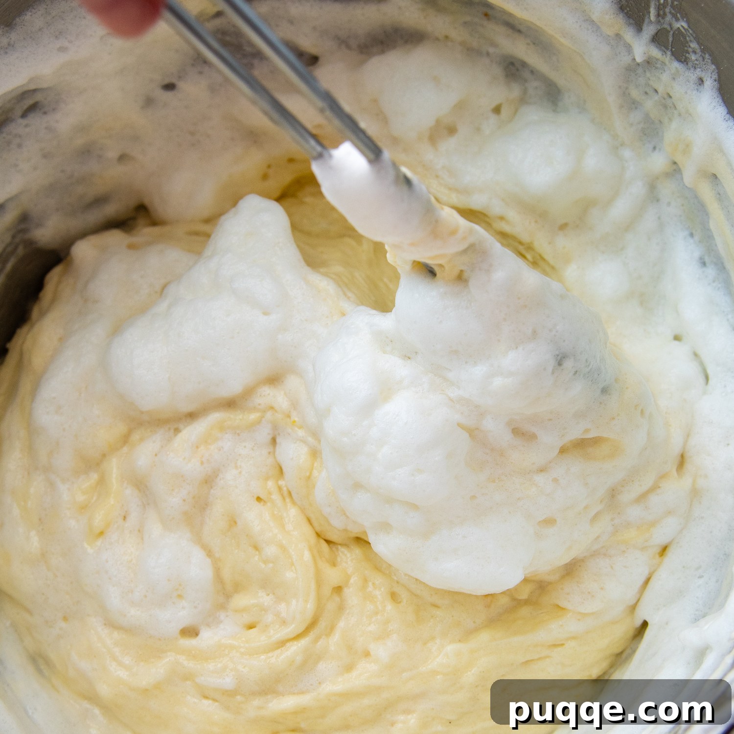 Decadently Moist Gluten-Free Coconut Lemon Curd Velvet Cake 7 Delicate egg whites being carefully folded into the cake batter, indicating the final stage of batter preparation for a light texture.