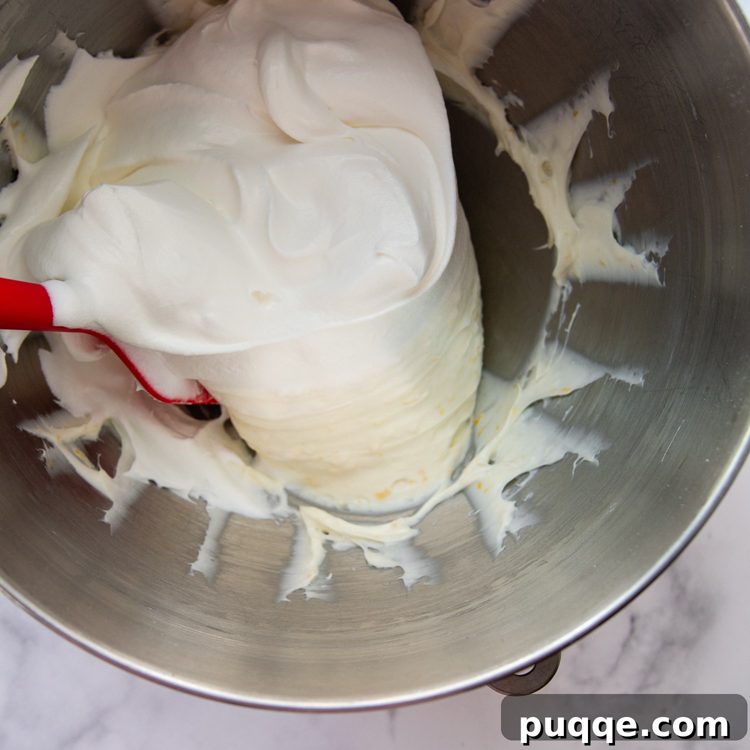 Decadently Moist Gluten-Free Coconut Lemon Curd Velvet Cake 8 Whipped topping being gently folded into the lemon cream cheese frosting, creating a light and airy texture.