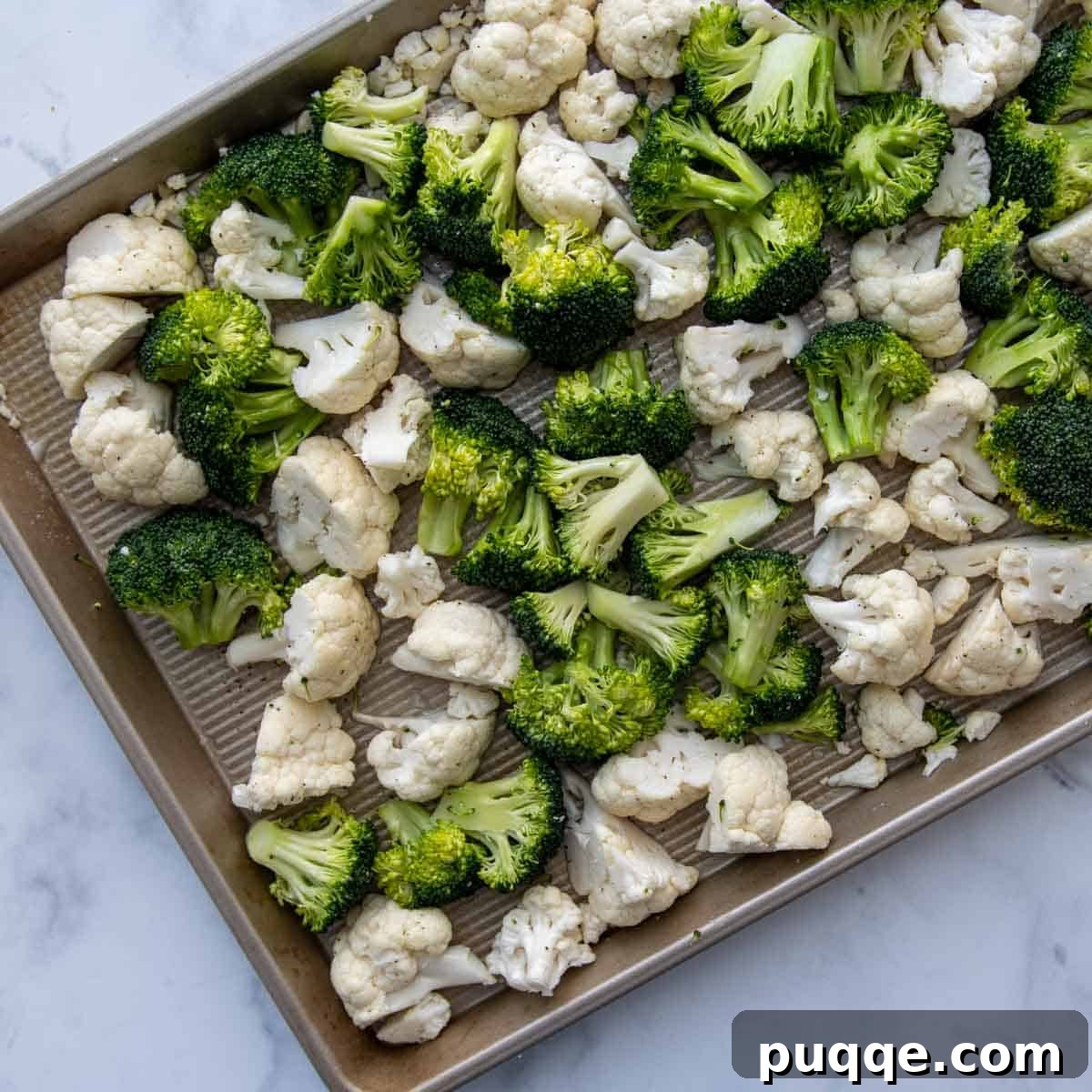 Fresh broccoli and cauliflower florets tossed with olive oil, salt, and pepper, spread evenly on a baking sheet, ready for roasting.