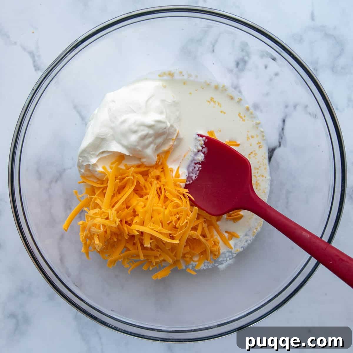 A bowl containing the creamy cheese sauce ingredients: sour cream, heavy cream, shredded cheddar cheese, and garlic powder, ready to be mixed.