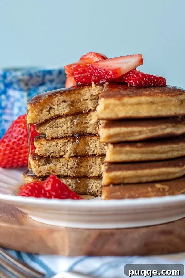 A stack of golden almond flour banana pancakes, artfully cut, with warm maple syrup cascading down the sides, presented on a white plate ready for a delightful breakfast.
