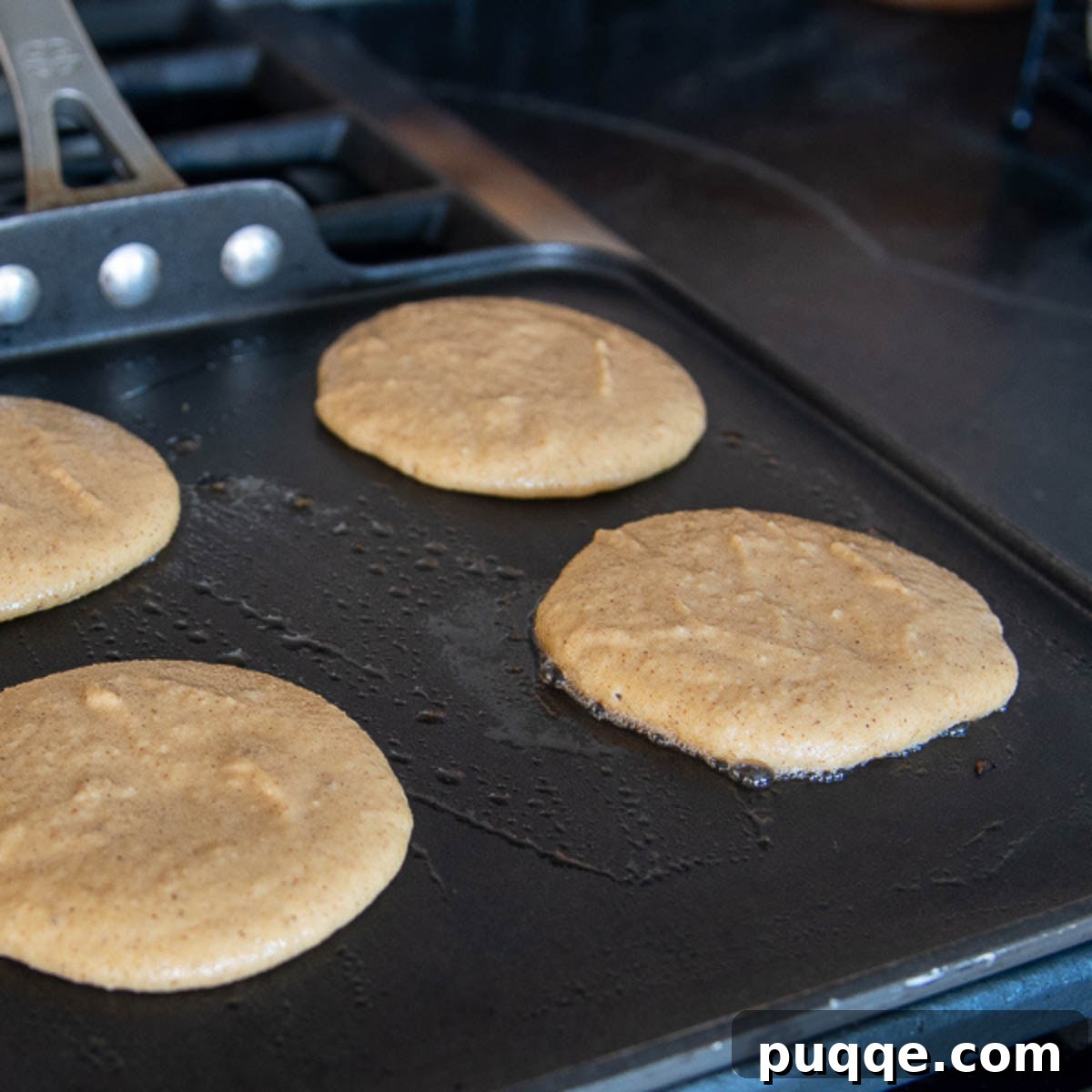 Several almond flour pancakes cooking on a hot griddle, showing the gentle browning and bubbling of the batter as they cook.
