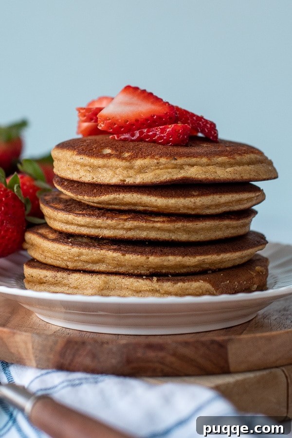 A beautiful stack of almond flour pancakes served on a pristine white plate, adorned with freshly sliced vibrant red strawberries on top, creating an inviting and healthy breakfast.