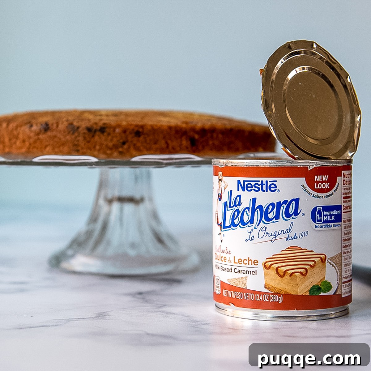 a can of dulce de leche in the foreground with a cake being assembled in the background.