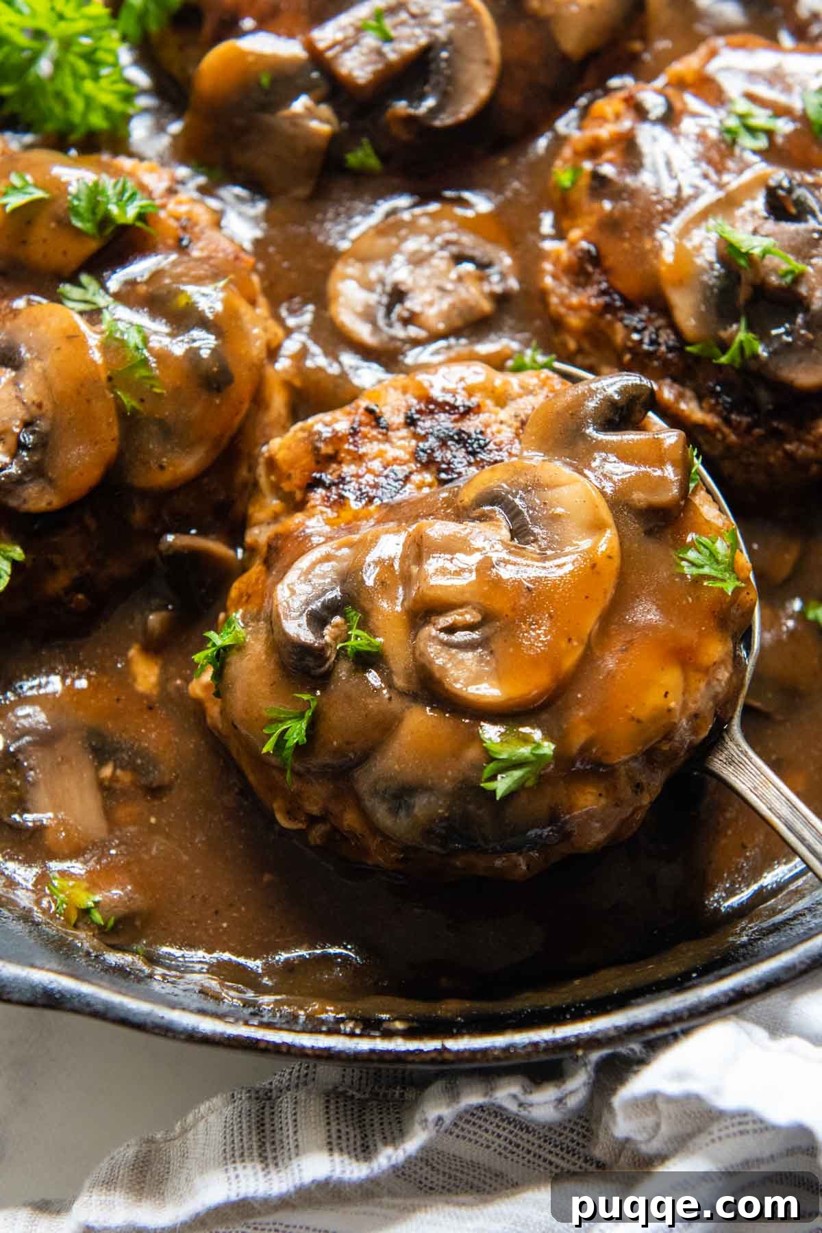 A spoon lifting a gluten-free Salisbury steak with mushrooms from a skillet.