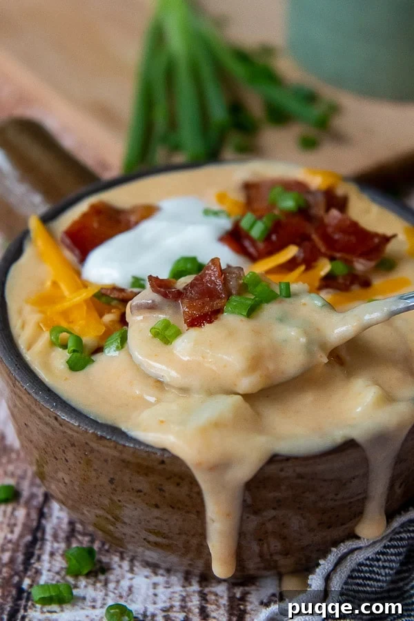 Close-up of a spoon lifting out a spoonful of creamy Instant Pot potato soup, laden with toppings.