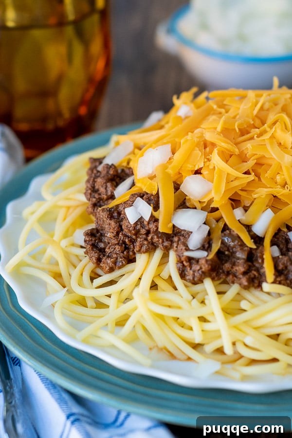 Close-up of rich meat sauce over spaghetti with a generous topping of cheese, and a cup in the background.