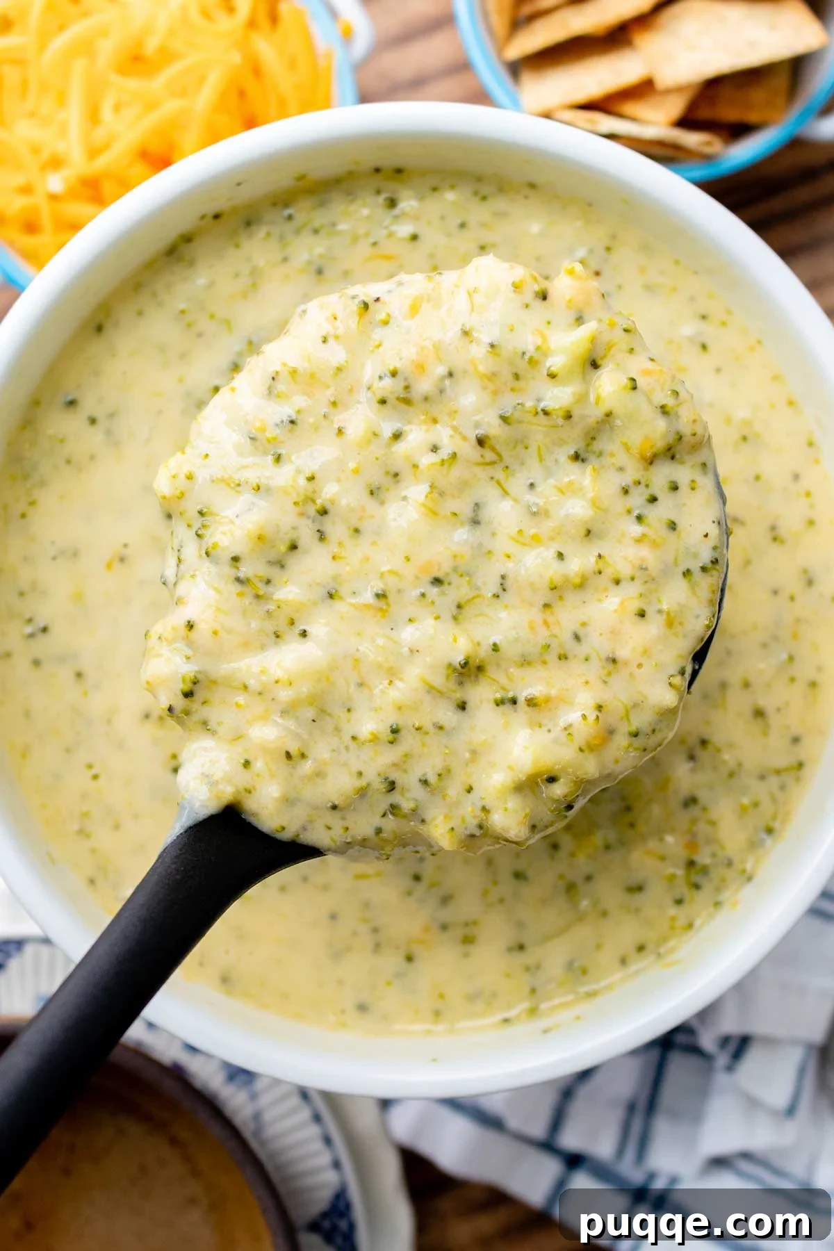 Overhead shot of a ladle holding up a creamy and cheesy broccoli cheddar soup.