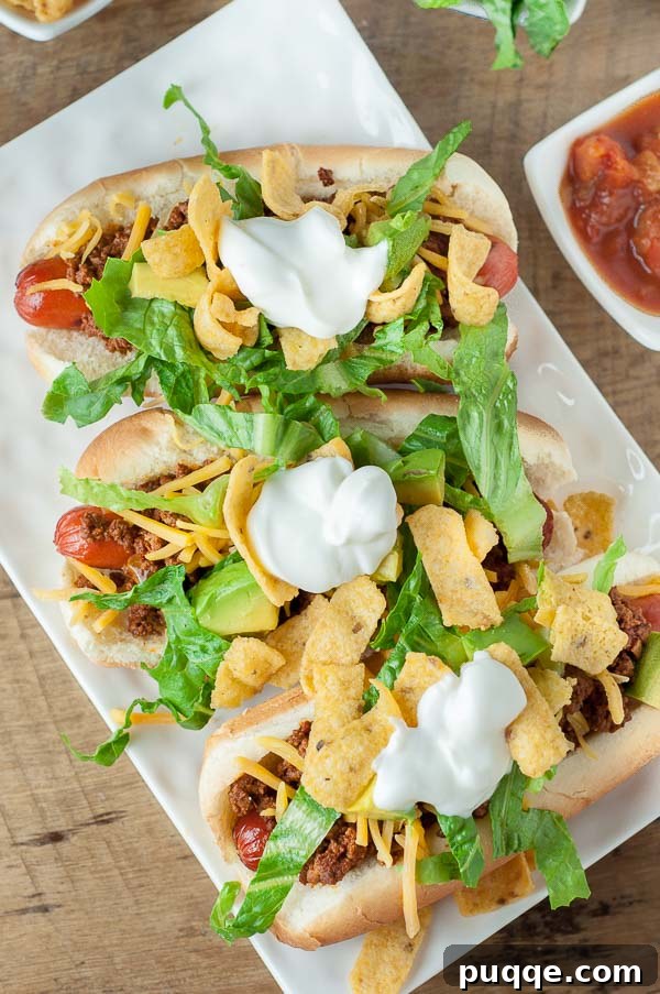 An overhead shot of vibrant Mexican hot dogs on a white rectangular plate, with a small dish of salsa nearby.