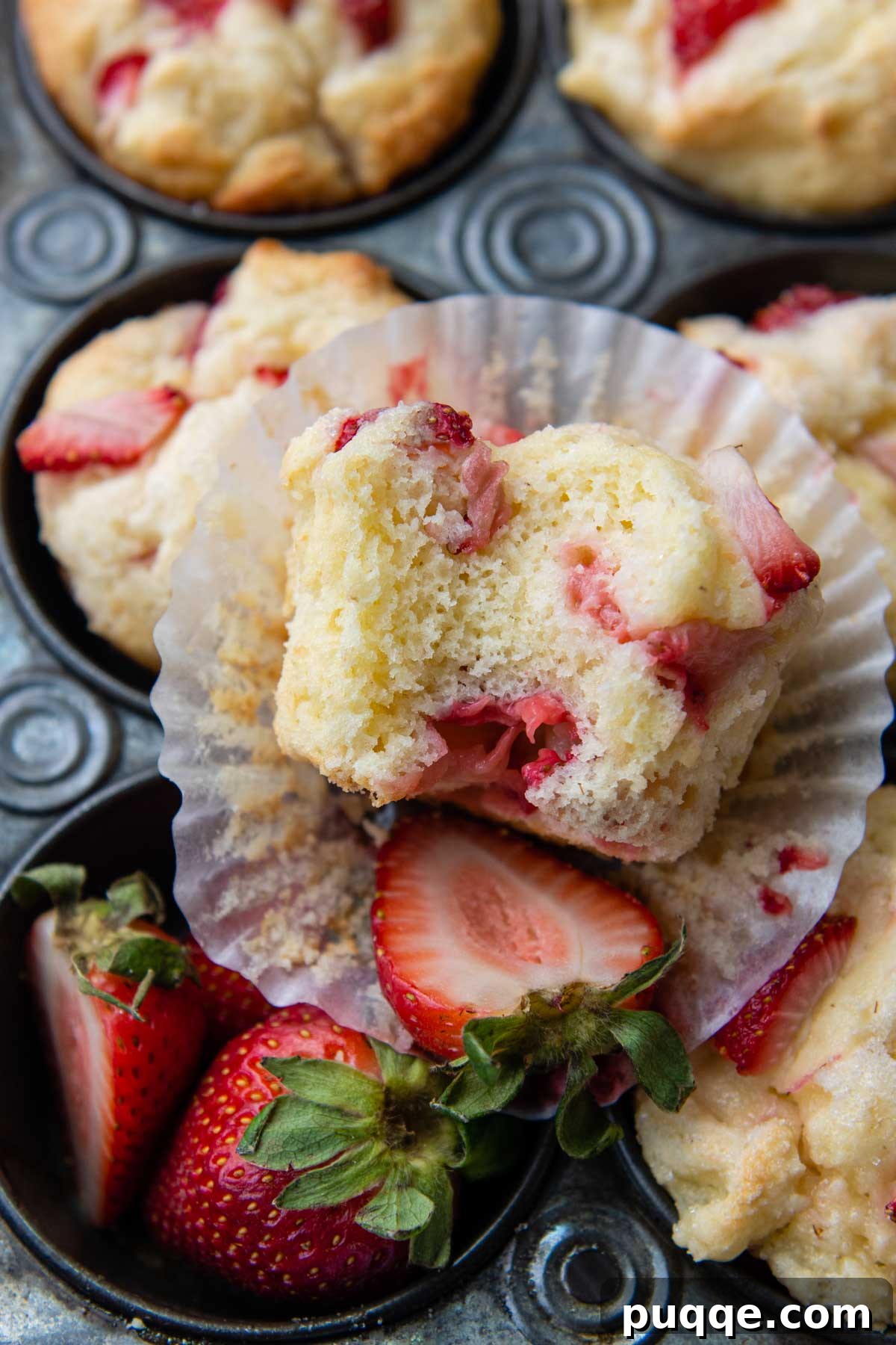 A delicious gluten-free strawberry muffin, bitten into, resting in its paper liner.