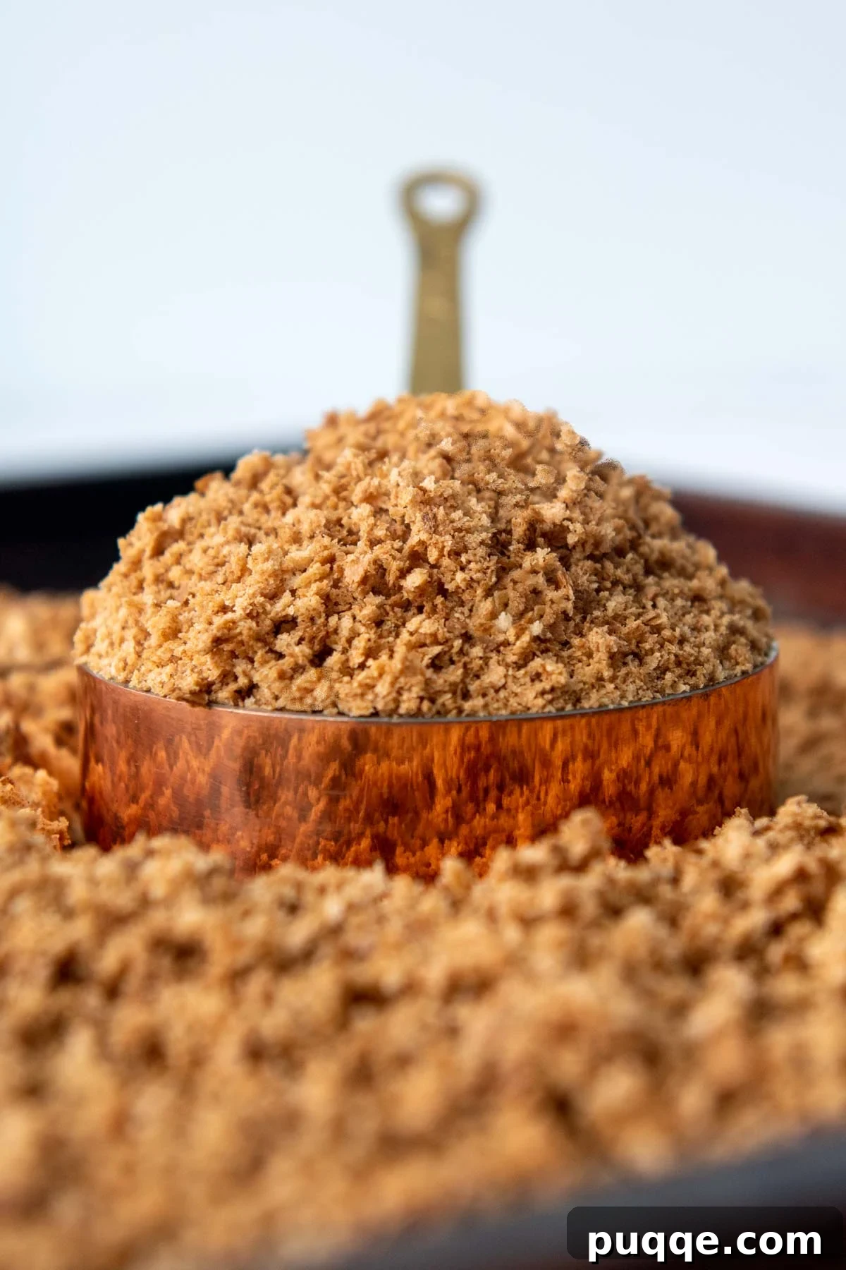 A heaping scoop of bread crumbs in a copper measuring cup, showcasing the golden texture of homemade gluten-free breadcrumbs.