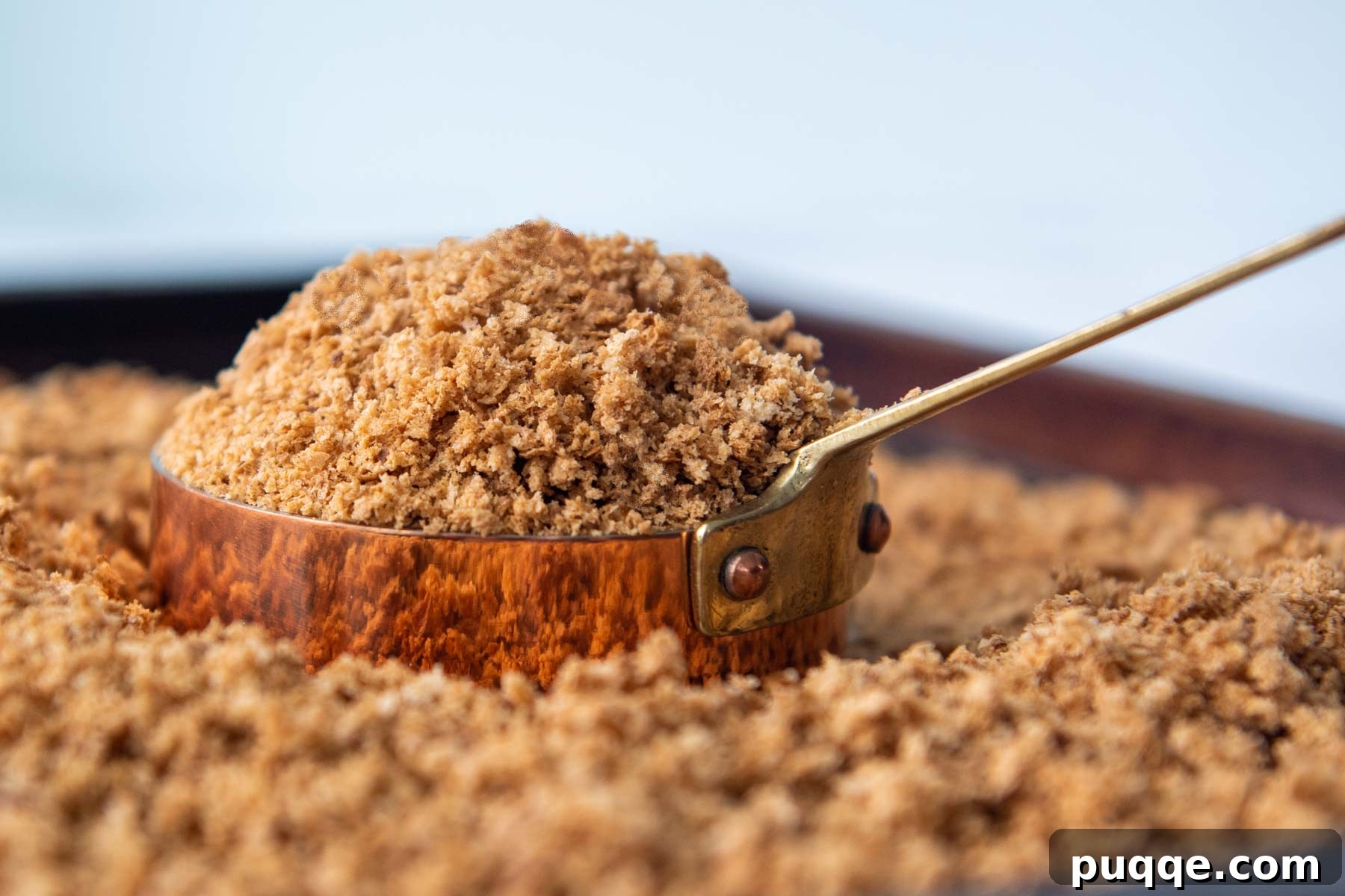 A copper measuring cup filled with golden, homemade gluten-free breadcrumbs, ready for culinary use.