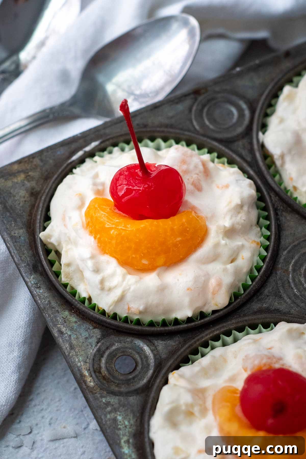 Frosty Fruit Medley 5 Top view of frozen fruit salad cups in a muffin tin, garnished with orange segments and maraschino cherries.