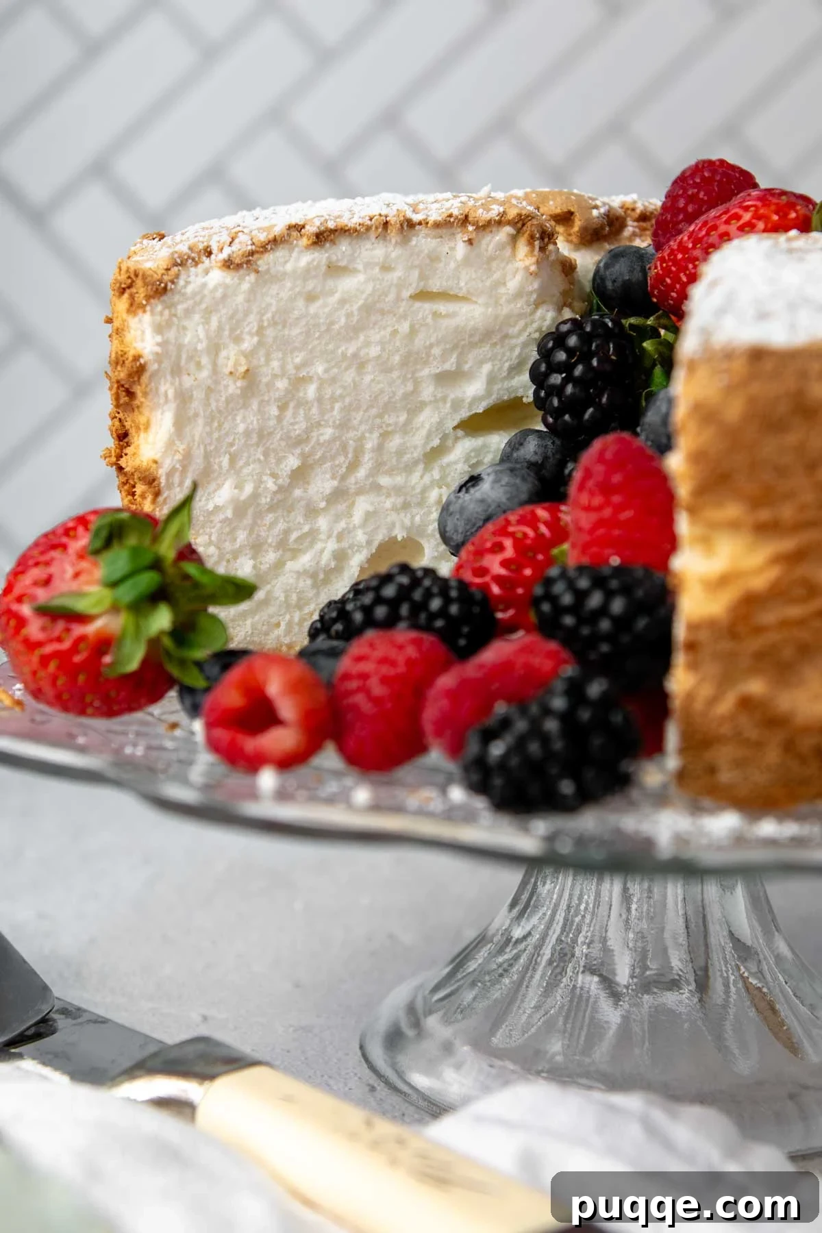 Pillowy Soft Gluten-Free Angel Food Delight 2 A beautifully sliced gluten-free angel food cake on a cake stand, garnished with fresh berries.