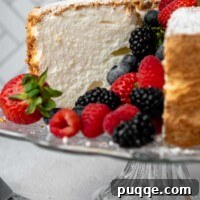 A sliced gluten-free angel food cake on a stand, facing straight on with berries in the middle.