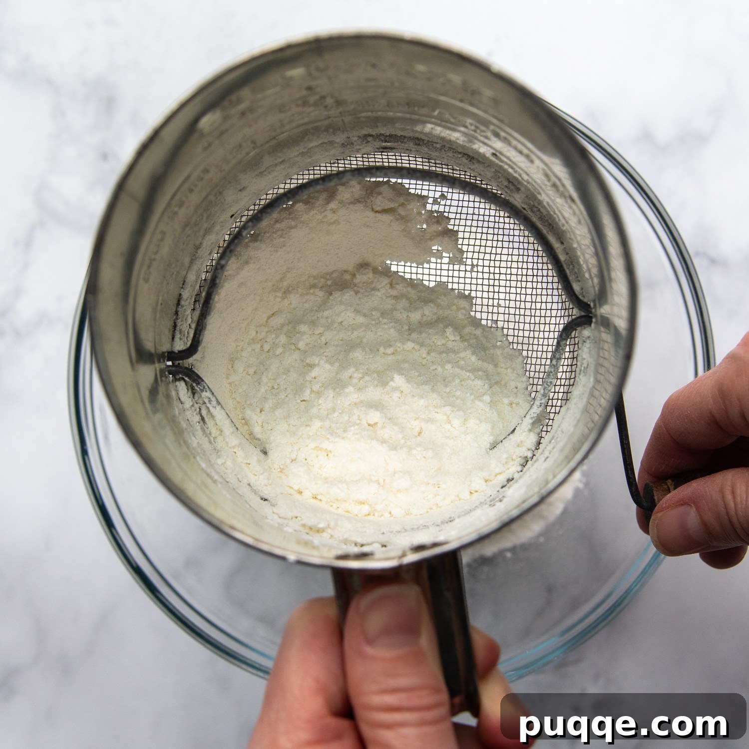 Pillowy Soft Gluten-Free Angel Food Delight 4 Sifting dry ingredients, including gluten-free flour and cornstarch, with a sifter.