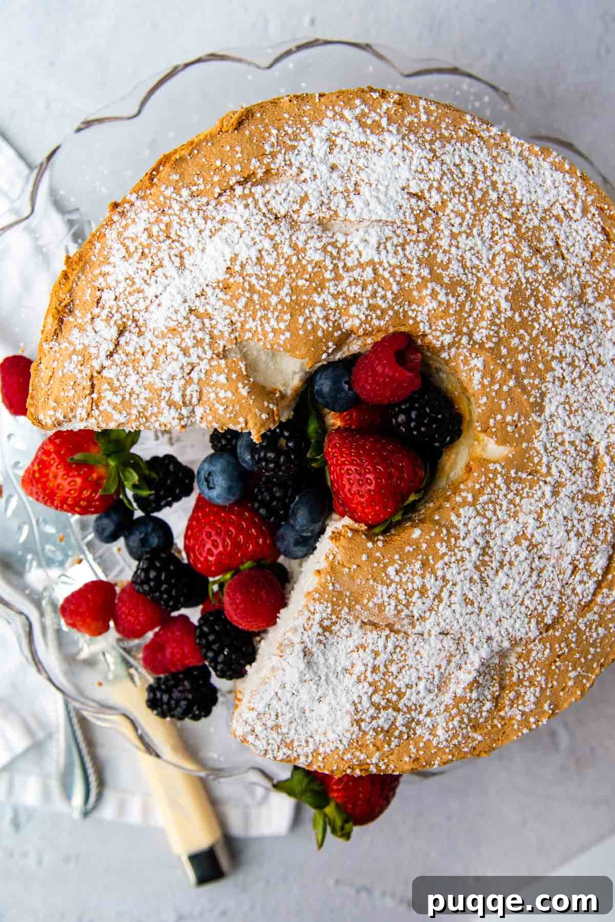 Pillowy Soft Gluten-Free Angel Food Delight 9 An overhead shot of a gluten-free angel food cake with fresh berries, with a cake knife nearby.