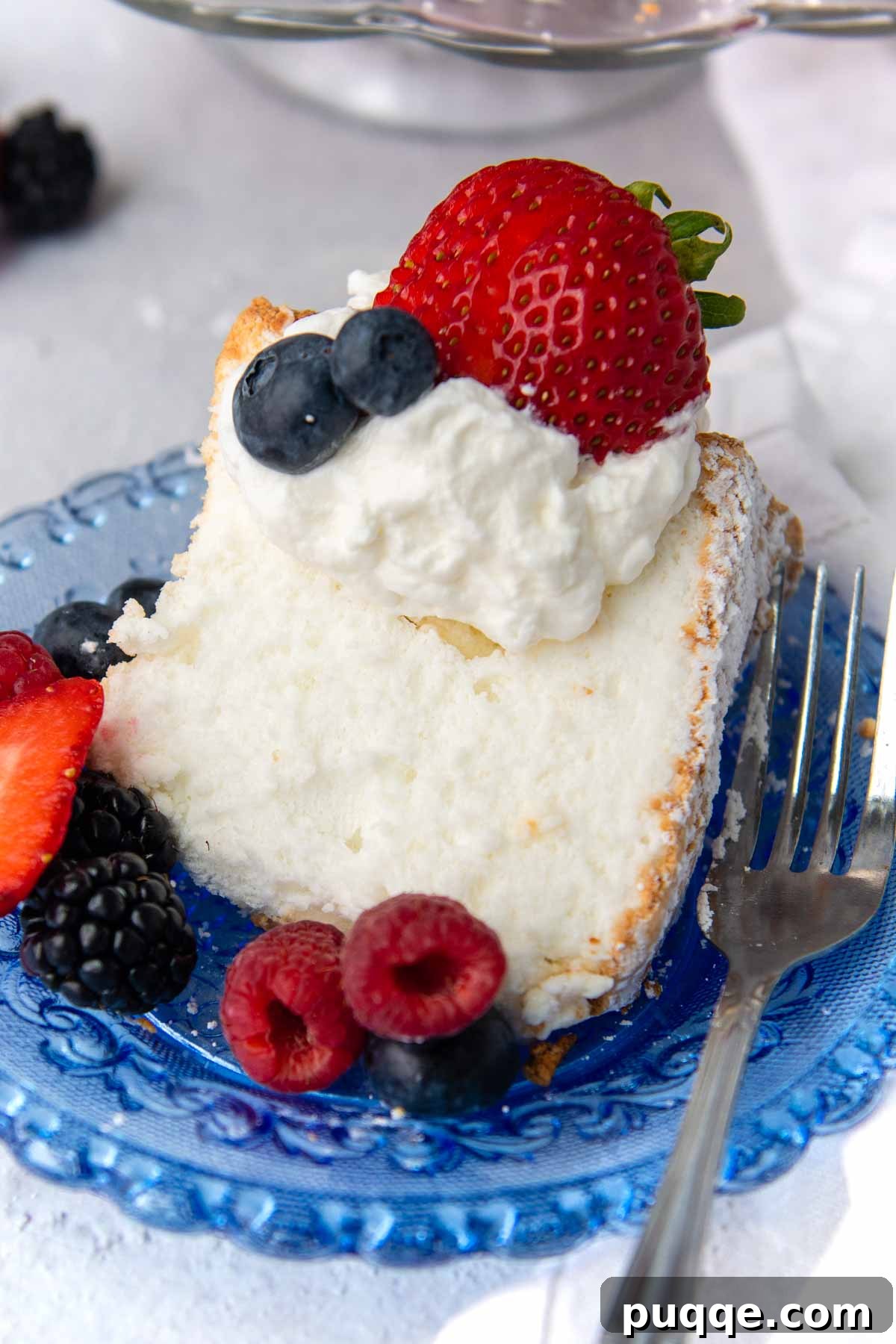 Pillowy Soft Gluten-Free Angel Food Delight 10 A slice of angel food cake on a blue plate, topped with whipped cream and fresh fruit.