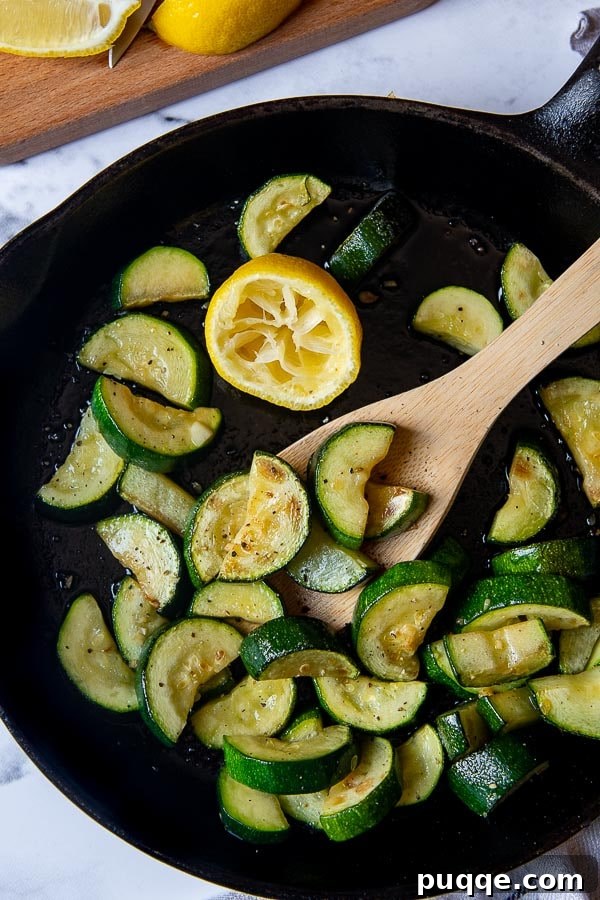 Bright Lemon Garlic Zucchini 4 overhead shot of vibrant green sauteed zucchini and yellow squash in a cast iron skillet, garnished with fresh lemon slices and herbs.