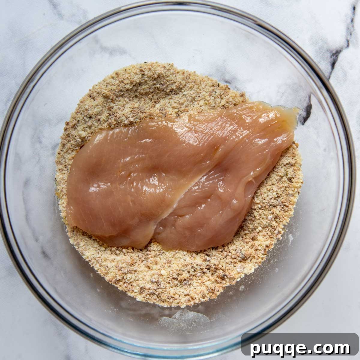 Oven-Crisp Gluten-Free Chicken Parmesan 4 raw chicken breast in a bowl of seasoned breadcrumbs.