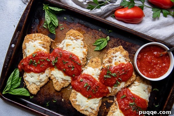 Oven-Crisp Gluten-Free Chicken Parmesan 6 overhead shot of a baking sheet of gluten free chicken parmesan with fresh basil scattered around and a cup of marinara