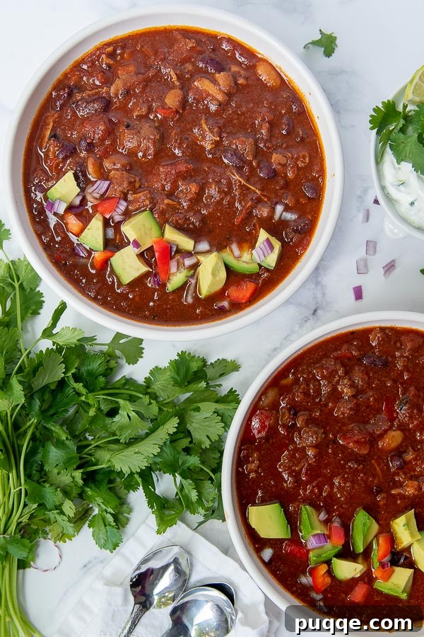 Signature Red Chicken Chorizo Chili 3 Overhead shot of two bowls of chorizo chili, garnished with avocado slices.