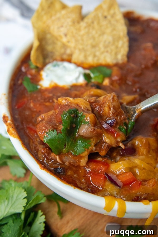 Signature Red Chicken Chorizo Chili 8 A spoon dipping into a bowl of chicken and chorizo chili, showcasing its rich texture and toppings.