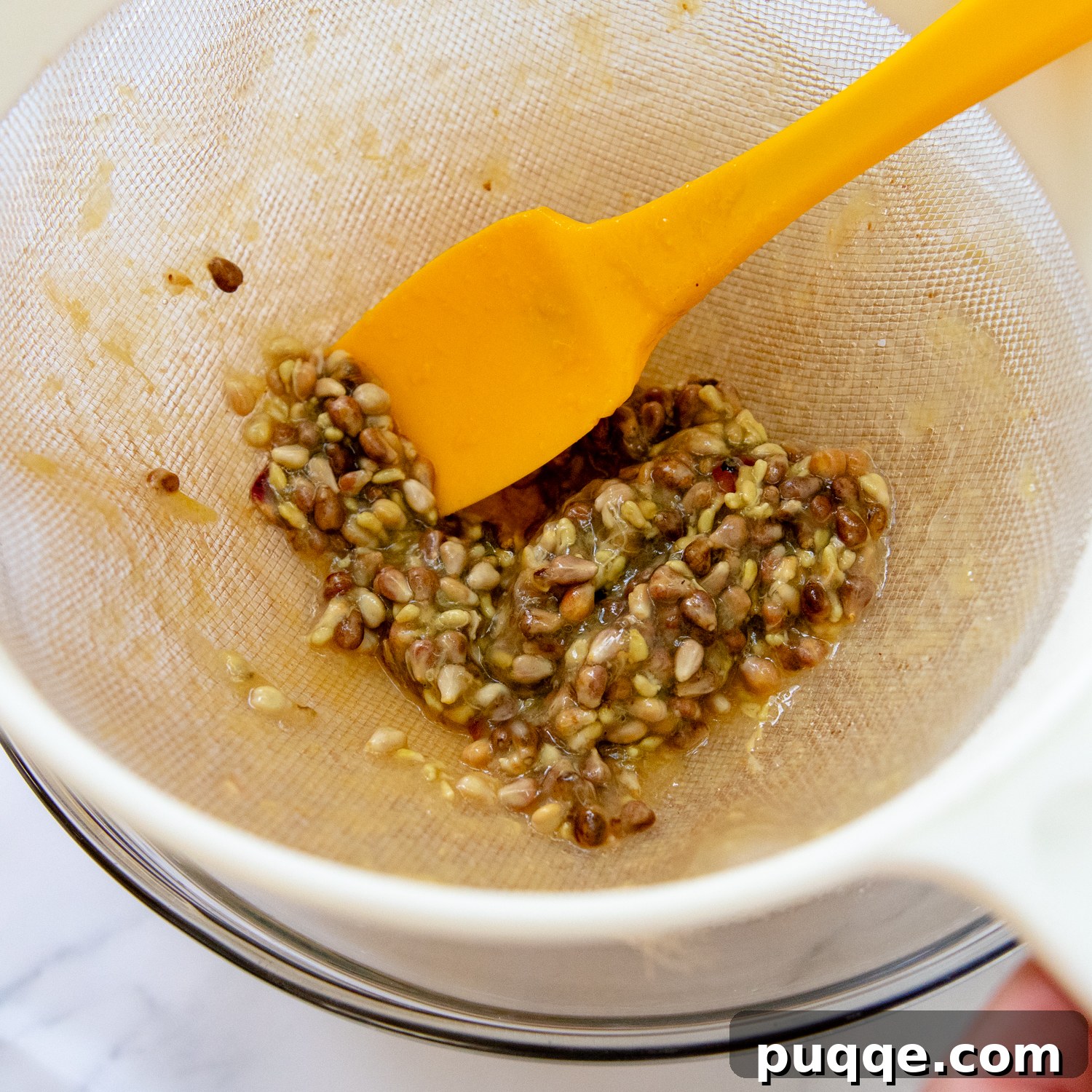 Classic Concord Grape Streusel Pie 5 Only grape seeds remaining in a mesh strainer, with a yellow spoon demonstrating the thoroughness of the straining process.