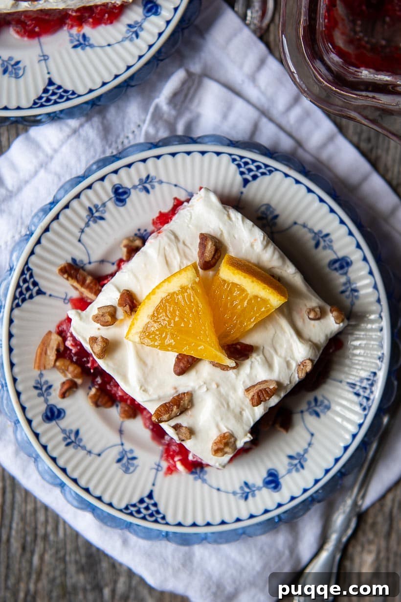 Classic Cranberry Raspberry Gelatin Mold 6 Overhead shot of a slice of cranberry jello salad on a plate, topped with nuts and an orange slice.