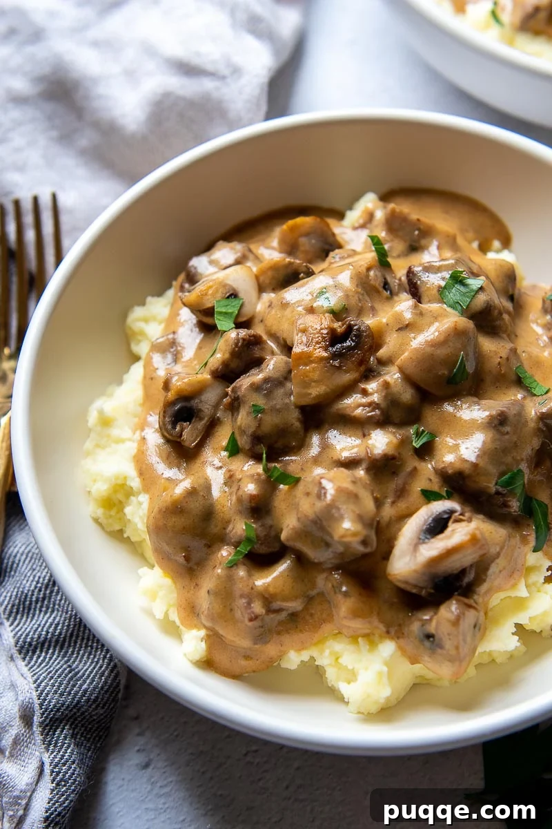 Tender Pressure Cooker Beef Stroganoff 2 Angled shot of a steaming bowl of pressure cooker beef stroganoff served elegantly over fluffy mashed potatoes, garnished with fresh parsley.