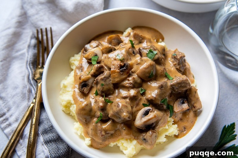 Tender Pressure Cooker Beef Stroganoff 6 Overhead shot of a beautifully set dinner table featuring a bowl of beef stroganoff, accompanied by elegant gold forks and knives.