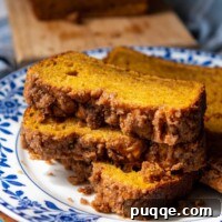 A stack of three slices of pumpkin bread with streusel topping on a blue and white flower plate