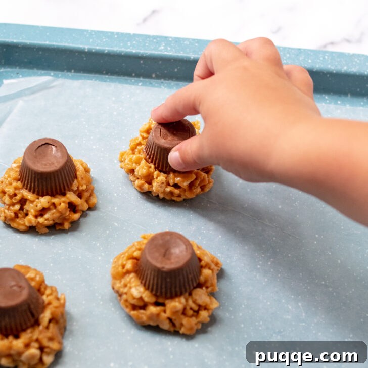 Ghoulishly Easy No-Bake Spider Treats 6 A child's hand carefully placing a peanut butter cup on top of a freshly scooped crispy rice cookie, forming the spider's body.