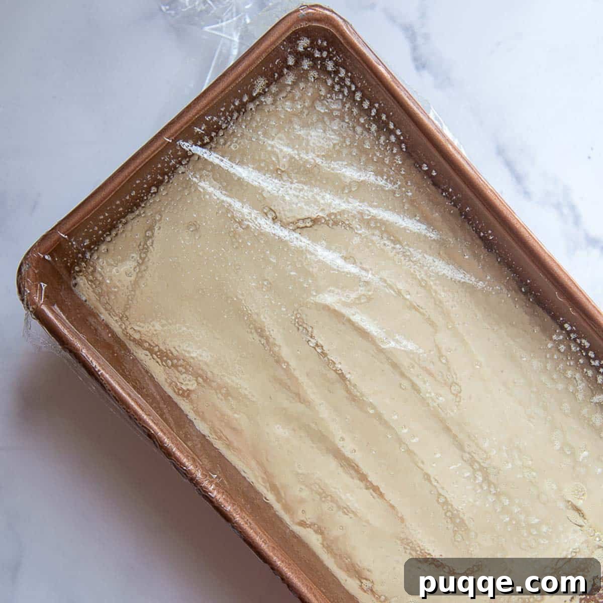 a bread pan with gluten-free dough rising, covered in plastic wrap