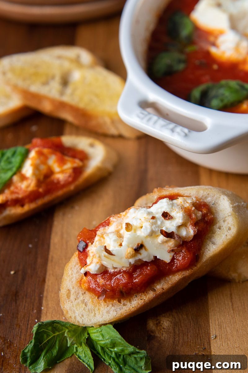 A piece of crostini with hot and creamy baked feta dip spread on it, showcasing the perfect texture.