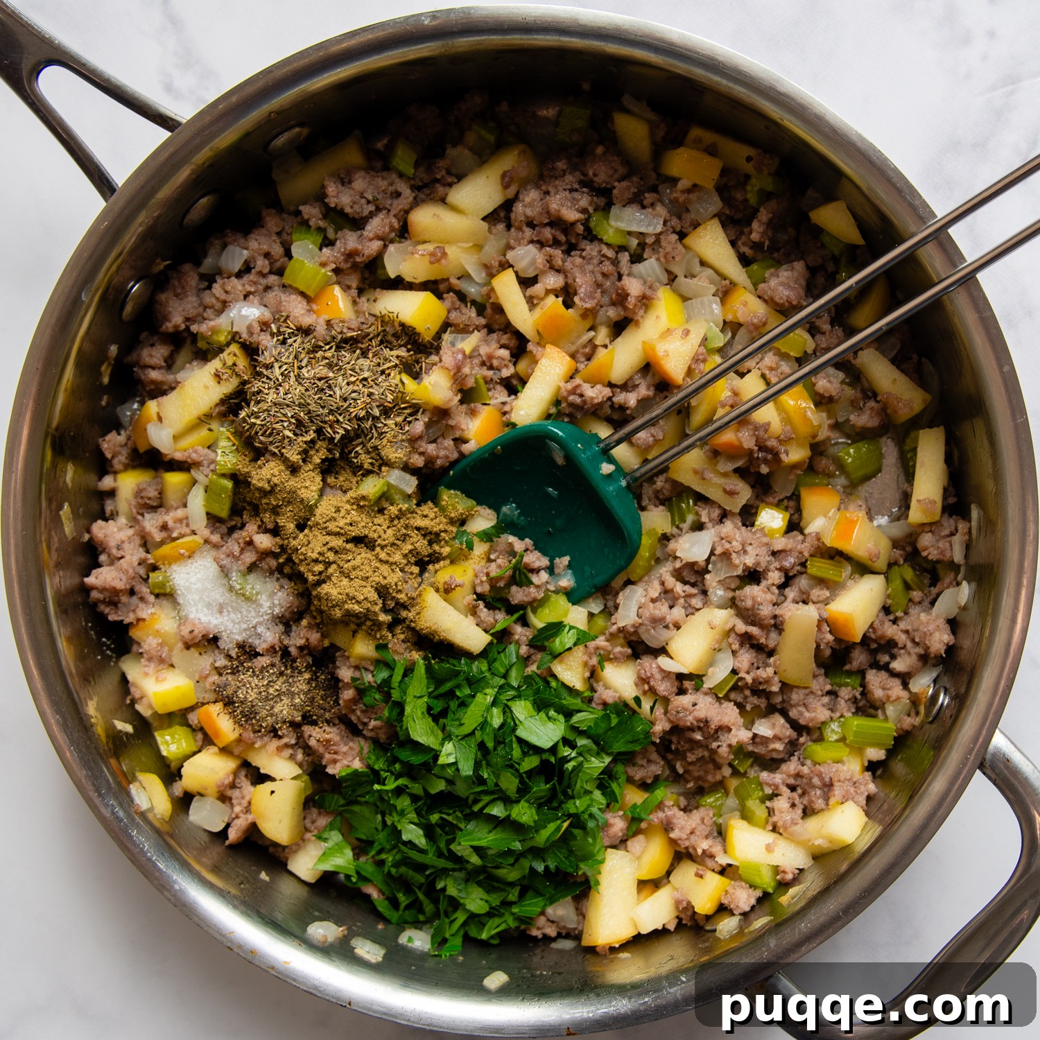 The savory stuffing mixture in a sauté pan, featuring browned sausage, cooked apples, vegetables, and fragrant herbs.