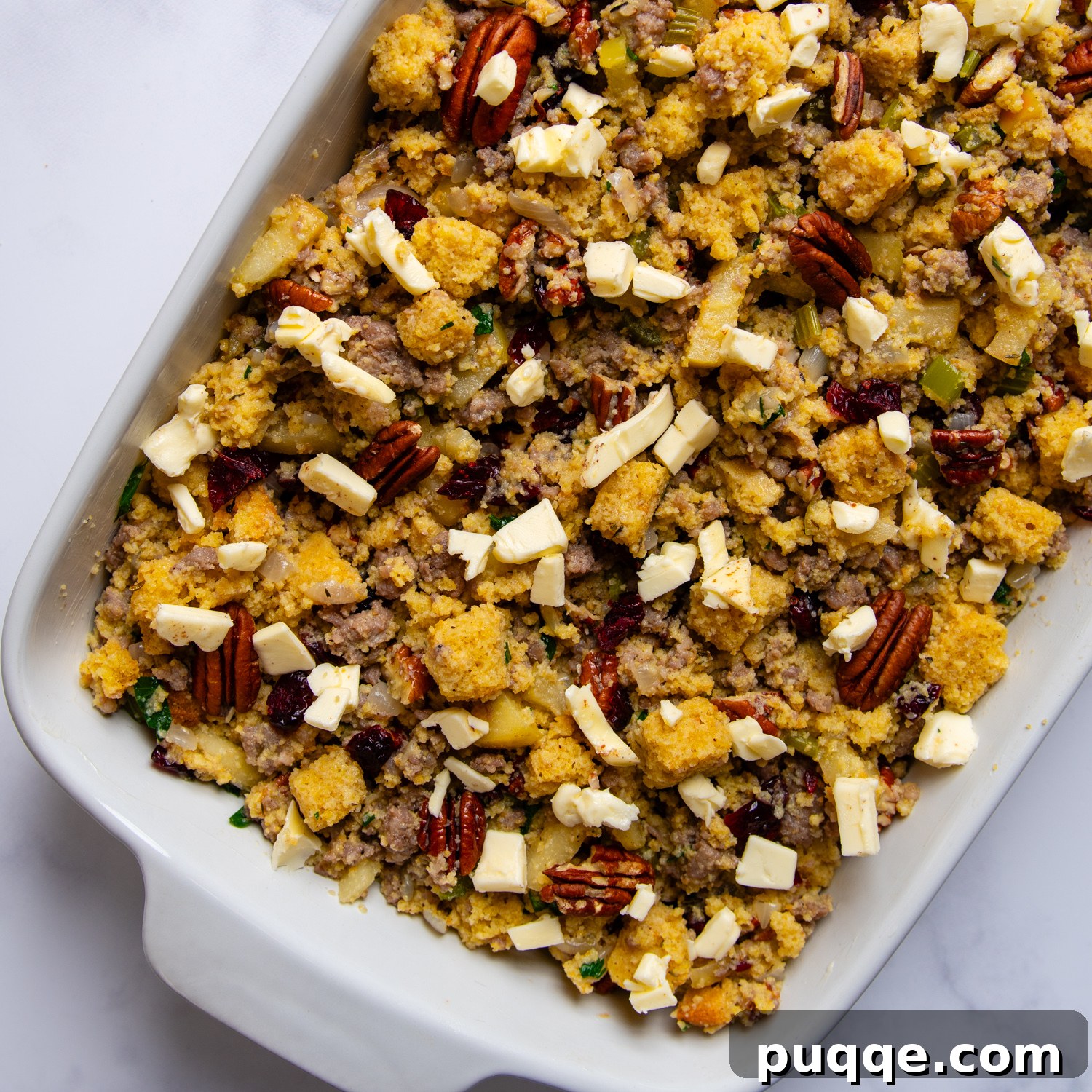 A casserole dish filled with gluten-free cornbread stuffing, topped with diced butter, ready for baking.