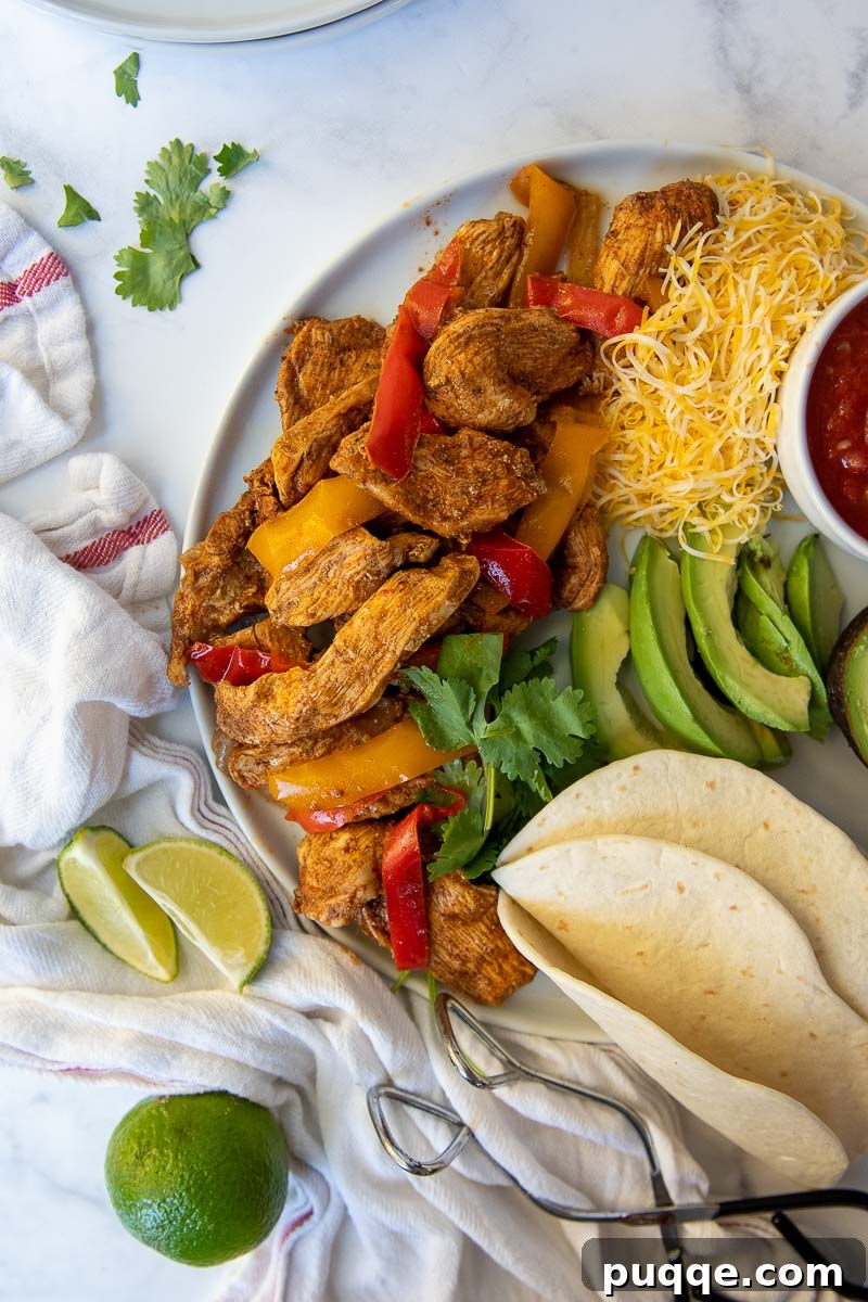An inviting close-up shot of chicken fajita meat, peppers, and onions, plated and ready to be served with various fresh toppings and tortillas.