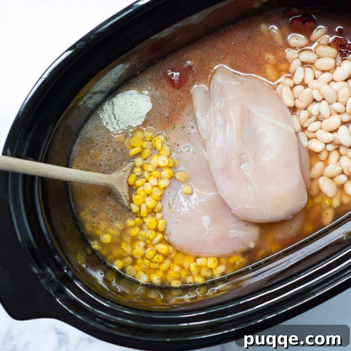 Award Winning Slow Cooker Buffalo Chicken Chili 4 All the initial ingredients for the buffalo chicken chili, including raw chicken, beans, tomatoes, broth, and seasonings, are carefully placed into a slow cooker.