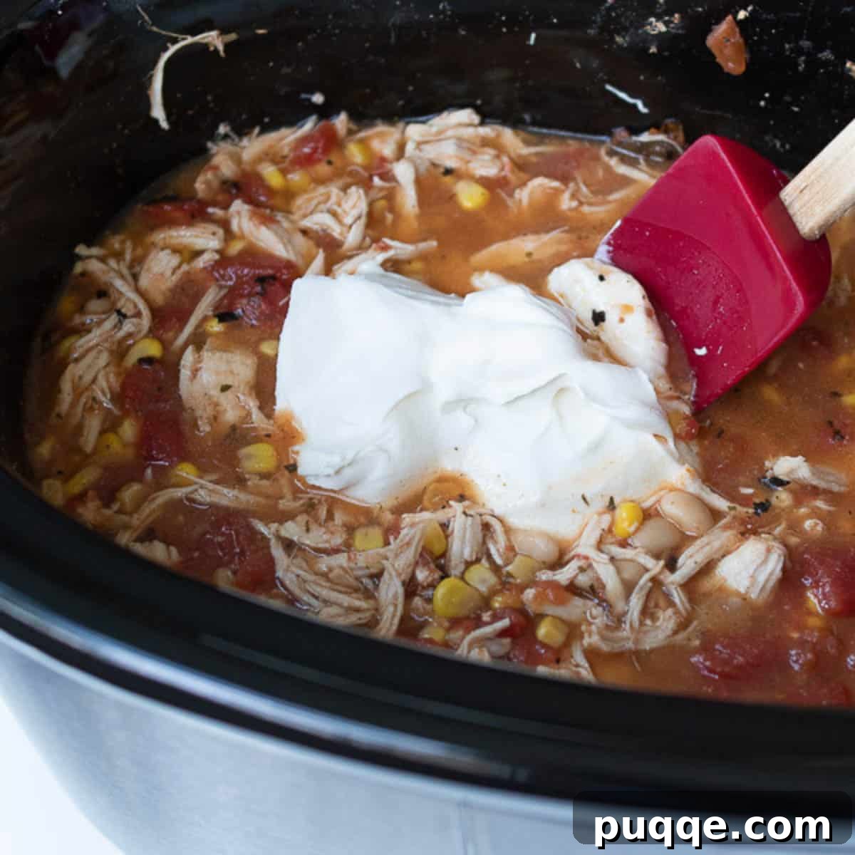 Award Winning Slow Cooker Buffalo Chicken Chili 6 A block of softened cream cheese is carefully added to the hot buffalo chicken chili in the slow cooker, preparing for the final creamy stir.