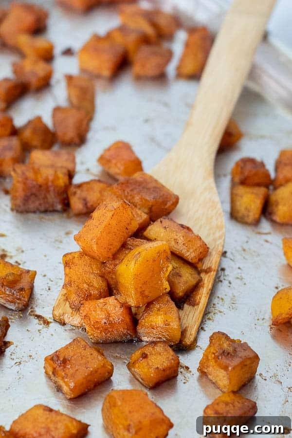A wooden spoon scooping perfectly roasted butternut squash from a baking sheet, showcasing its caramelized edges