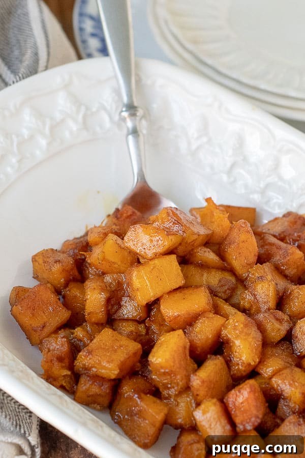 A spoon resting in a serving bowl filled with a generous portion of roasted butternut squash, ready to be enjoyed