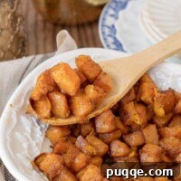 A wooden spoon lifting out a serving of roasted butternut squash from a bowl
