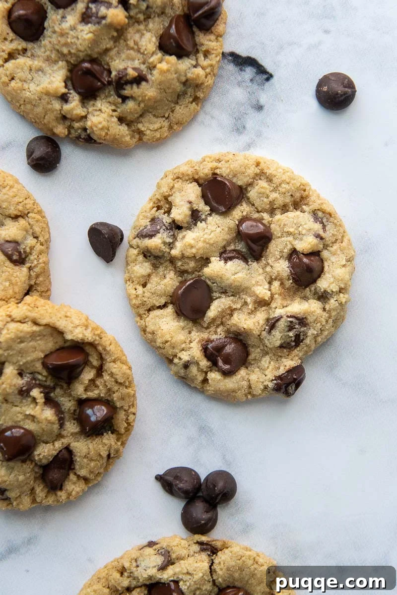 An overhead shot of freshly baked chocolate chip cookies laid flat on a surface, with additional chocolate chips scattered around for garnish.