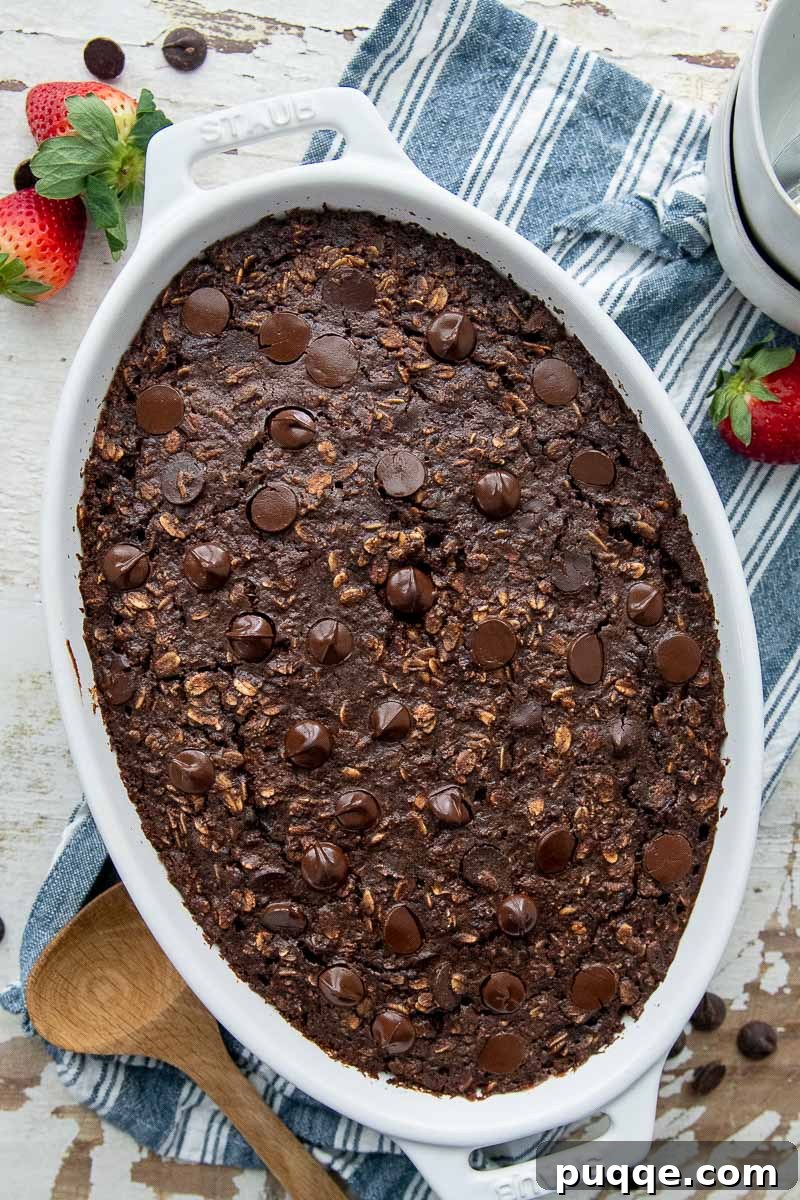An overhead shot of fudgy chocolate oatmeal baking in a white oval dish, perfectly paired with fresh, vibrant strawberries laying next to it, suggesting a delightful breakfast combination.