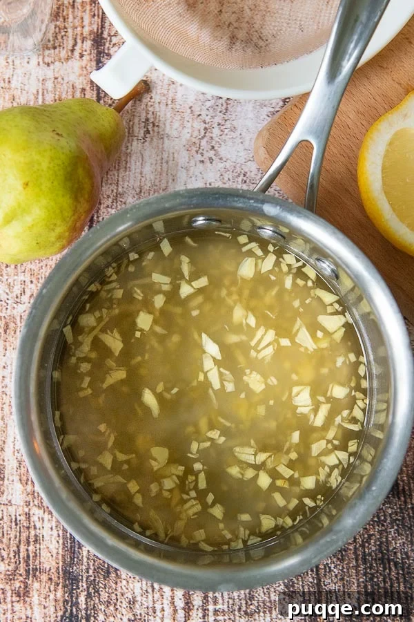 Spiced Pear Elixir 3 A saucepan filled with golden ginger syrup, featuring visible pieces of fresh chopped ginger simmering within. This image highlights the key ingredient for the Pear Ginger Cocktail and other delicious drinks.