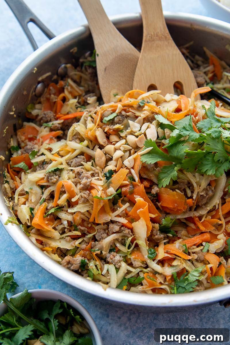 Close-up shot of the finished Unstuffed Egg Roll Bowl in a skillet, with wooden cooking utensils, highlighting the texture and vibrant ingredients.