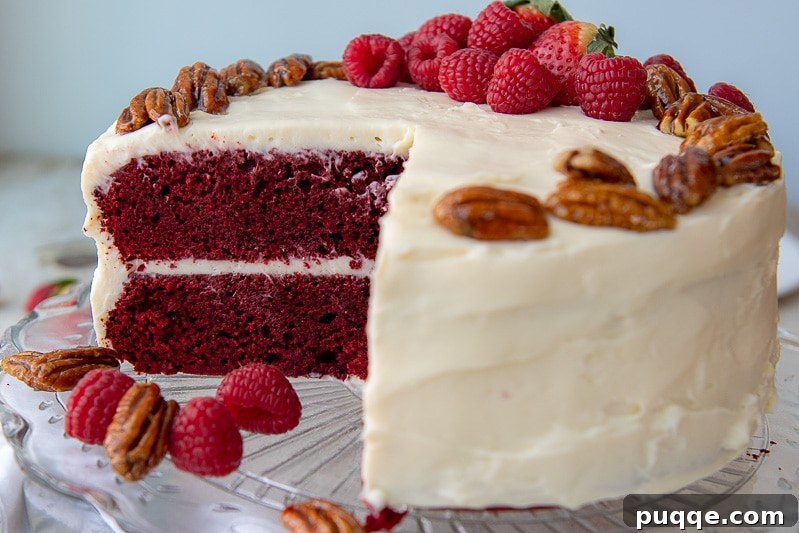 Decadent Gluten Free Red Velvet Pure Moist Perfection 7 A beautifully cut gluten-free red velvet cake on a clear glass platter, surrounded by fresh berries for a vibrant presentation.