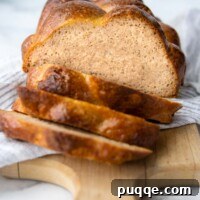 A sliced loaf of golden gluten-free challah bread, displaying its soft, inviting interior, resting on a white towel.