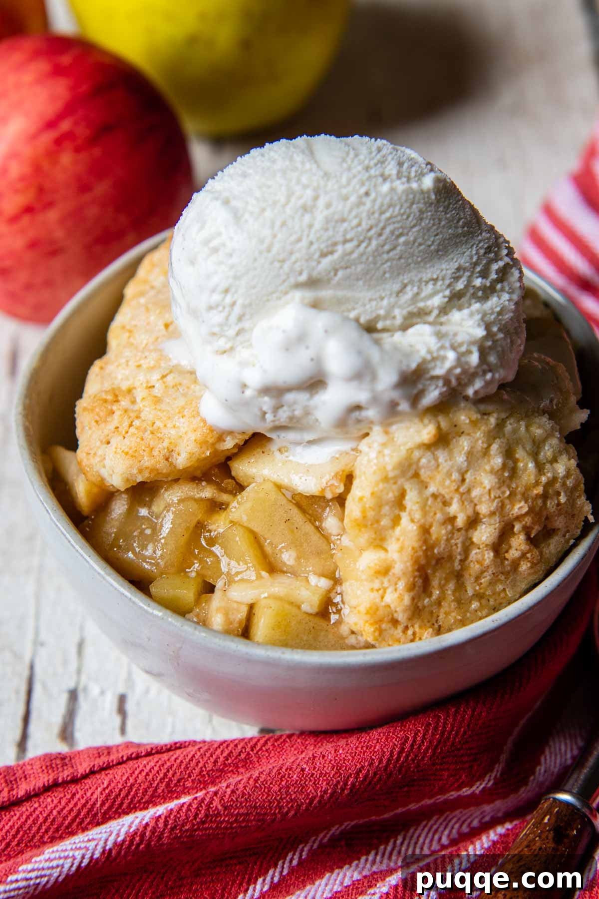 Easy Gluten Free Apple Cobbler with Fluffy Biscuit Topping 2 a serving of gluten-free apple cobbler in a white bowl with apples in the back ground